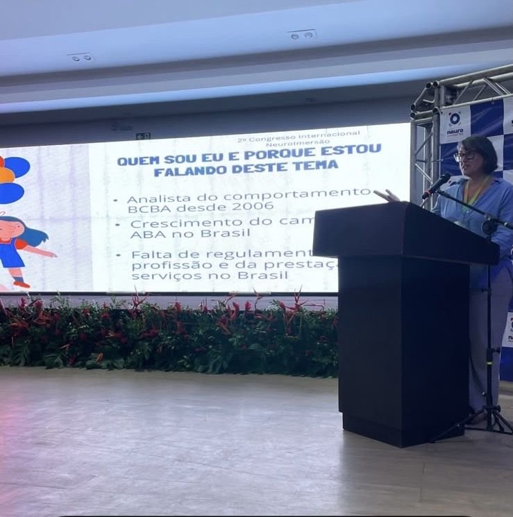 Valeria Parejo ao púlpito, diante do telão com o slide Quem sou eu e porque estou falando deste tema
